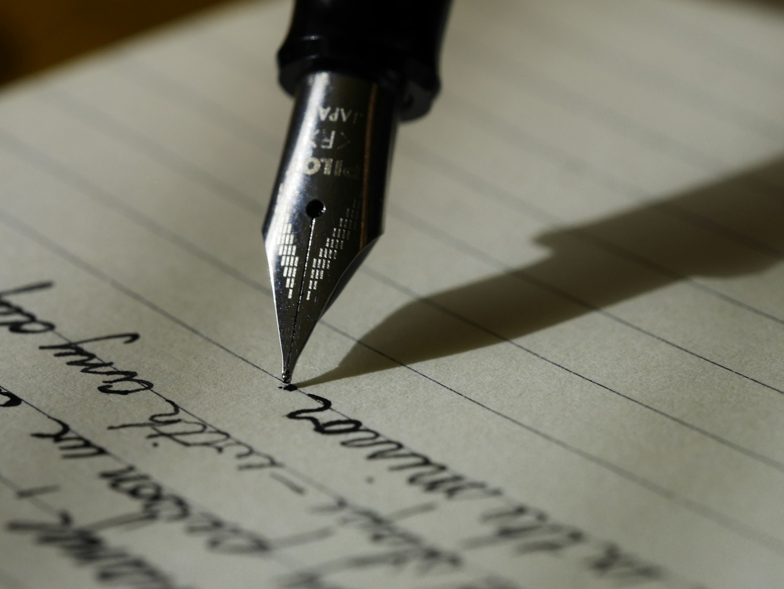 Una pluma estilográfica a medio trazo escribiendo cursiva en papel rayado