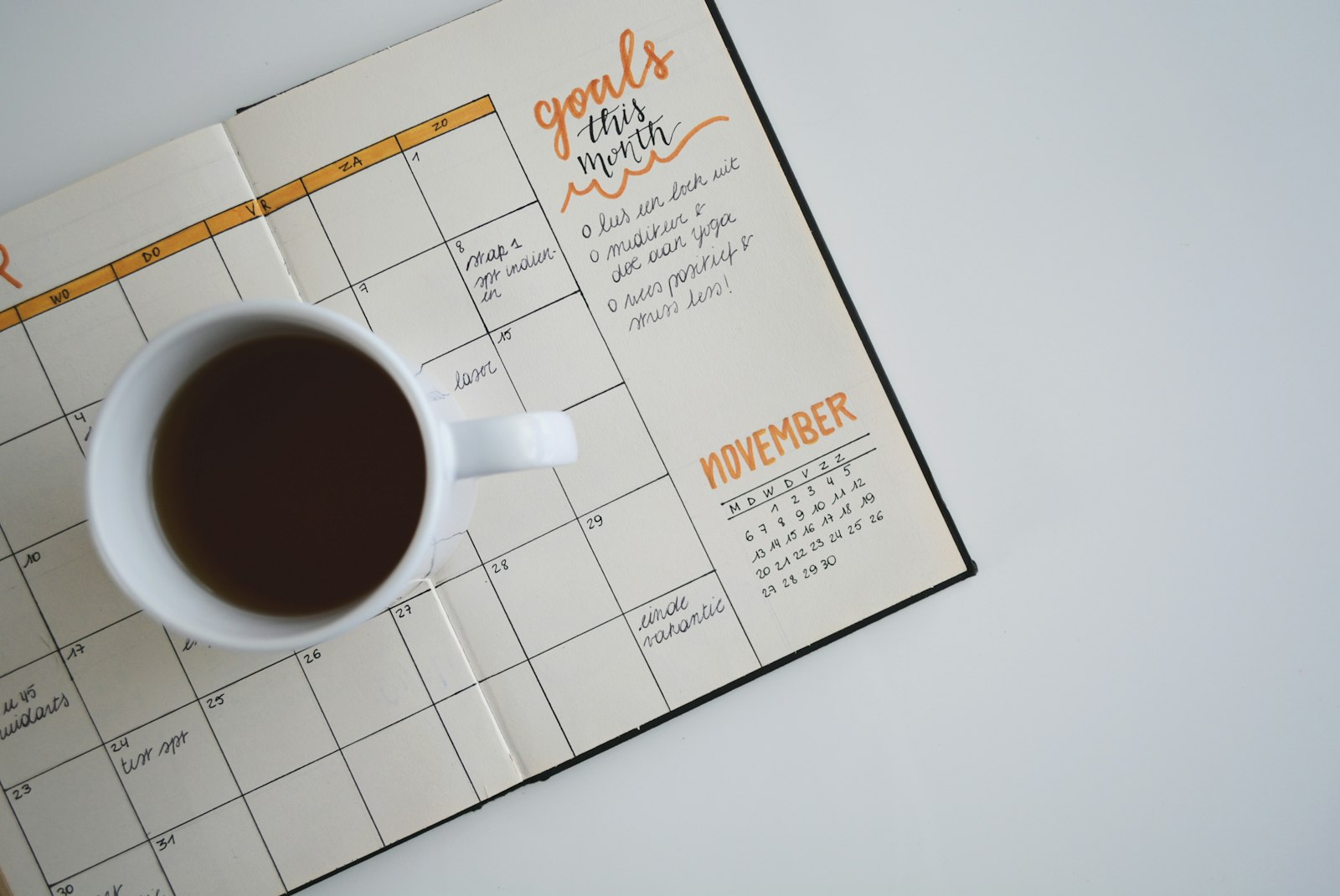 Una agenda mostrando un calendario mensual en blanco con metas escritas a mano junto a una taza de café